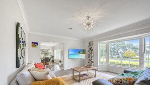 Una sala moderna con un sofá, una mesa de centro y un televisor. Hay un ventanal con vistas a la vegetación y a la playa.