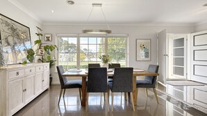 Un comedor moderno con una mesa de madera y seis sillas, ventanas amplias con vistas a la vegetación, y un armario de color claro con objetos decorativos.