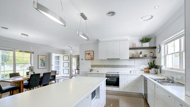 Una cocina moderna con armarios blancos, una isla grande y un comedor con sillas.