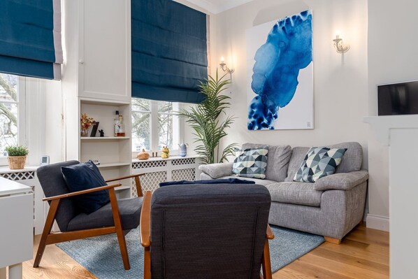 A modern living room with a grey sofa, two armchairs, a blue abstract painting, and a potted plant.