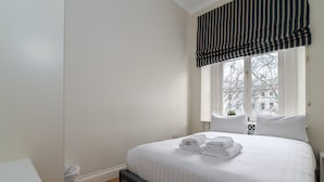 Ein Schlafzimmer mit einem großen Bett, weißer Bettwäsche, einem Fenster mit gestreiften Vorhängen und Blick auf Bäume.