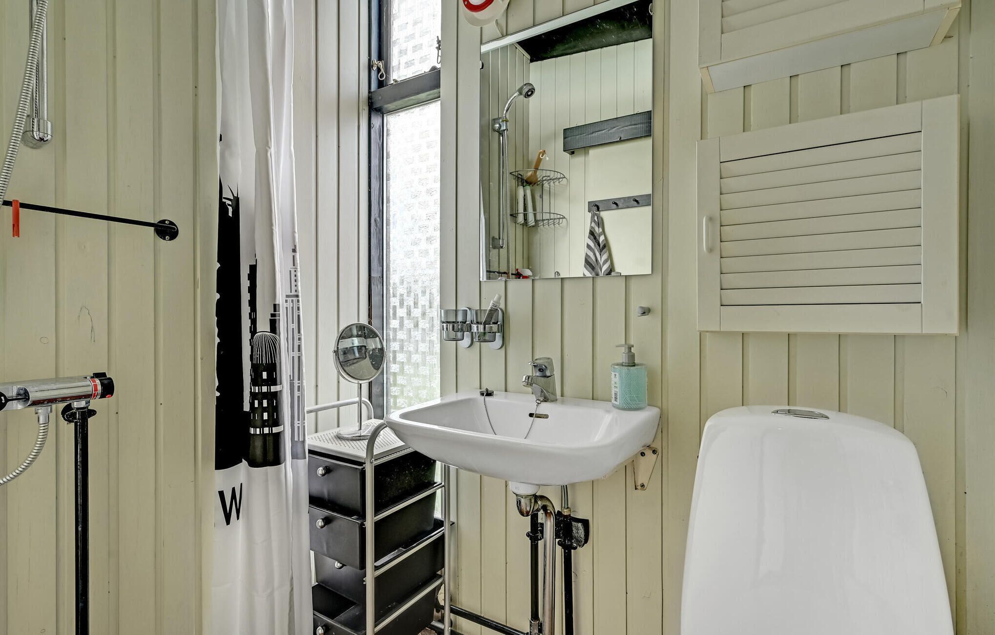 Une salle de bain avec un lavabo blanc, un miroir, une douche et des toilettes. Il y a un porte-serviettes au-dessus du lavabo et une serviette qui y est accrochée.
