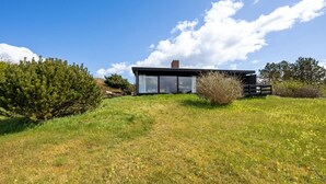 Ett modernt hus med stora glasfönster, omgivet av en gräsklädd äng och träd.