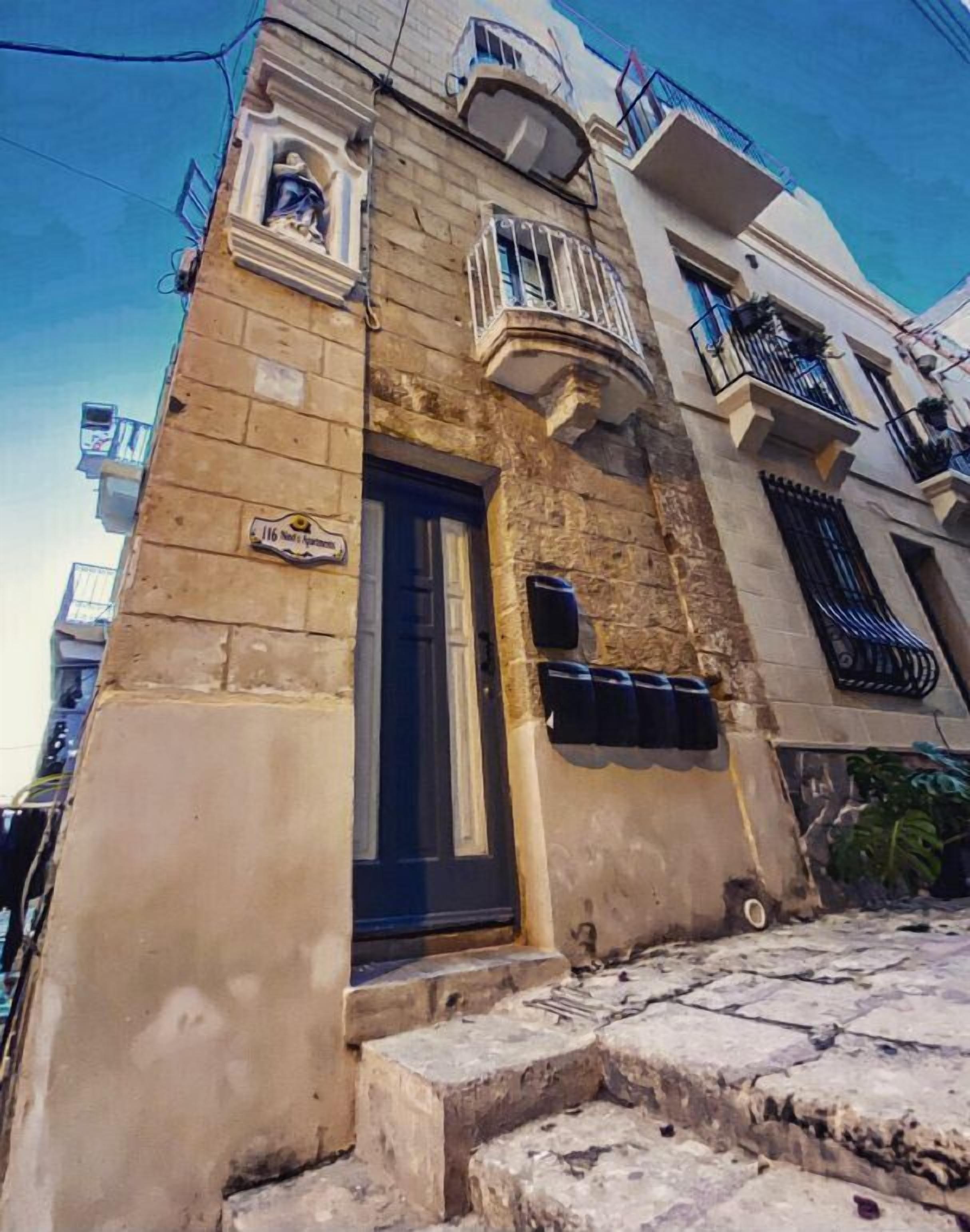 A building with a stone facade, a black door, and a small balcony with a metal railing.