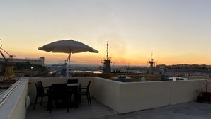 A rooftop terrace with a table and chairs, an umbrella, and a view of the city skyline at sunset. - Malta Suites 4 terrace (Isla)