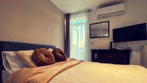 A hotel room with a bed, a flat-screen TV mounted on the wall, and an air conditioning unit. - Malta Suites 4 terrace (Isla)
