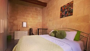 Een slaapkamer met een bed, een dressoir, een spiegel en een bakstenen muur.