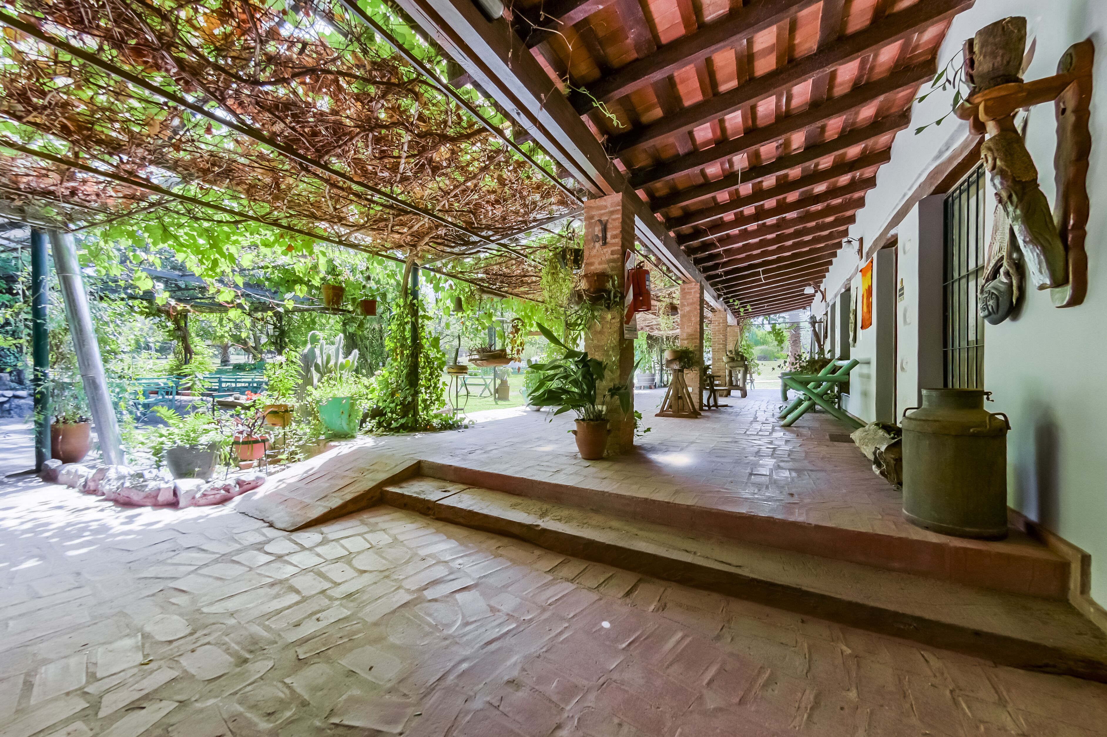 A covered outdoor area with a stone floor, potted plants, and a rustic wooden ceiling.