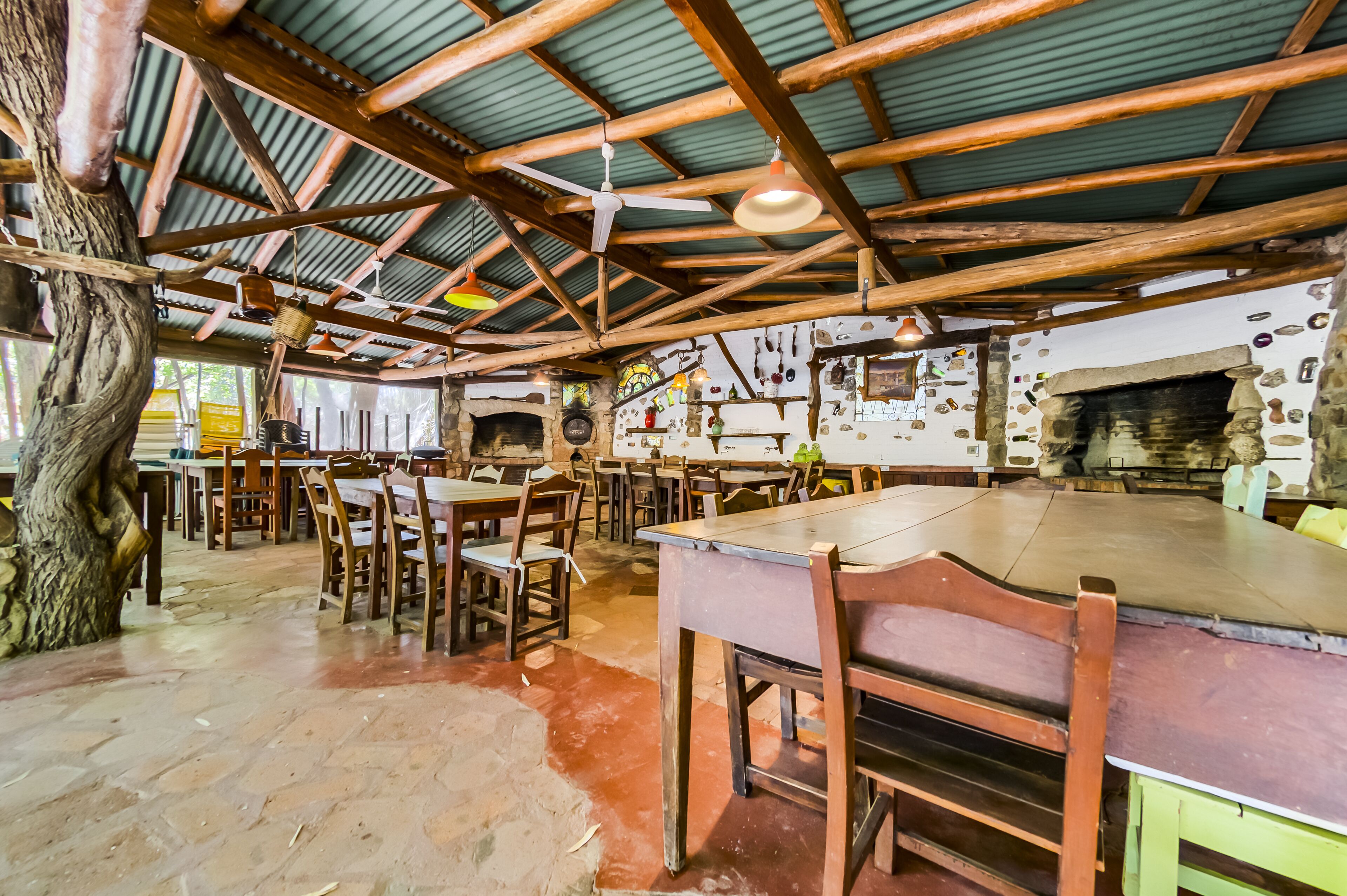 Un coin repas rustique avec des tables et des chaises en bois, une cheminée en pierre et un plafond aux poutres apparentes.
