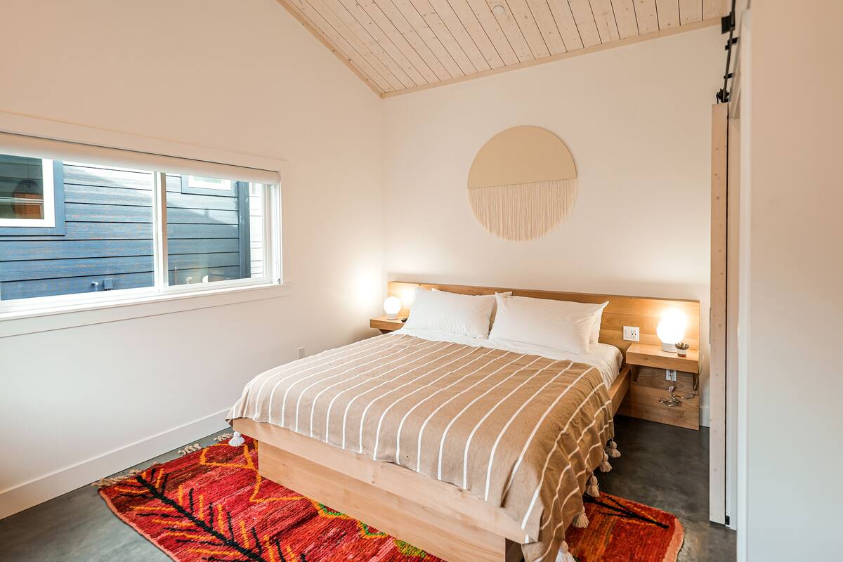 Une chambre à coucher comprenant un lit, des tables de chevet, une décoration murale ronde et une fenêtre avec des stores.