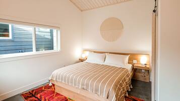 Une chambre à coucher comprenant un lit, des tables de chevet, une décoration murale ronde et une fenêtre avec des stores.