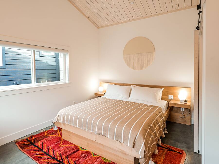 A bedroom with a bed, bedside tables, a round wall hanging, and a window with blinds.