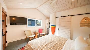 A bedroom with a bed, a TV, a window, a chair, a small table, and a wardrobe.