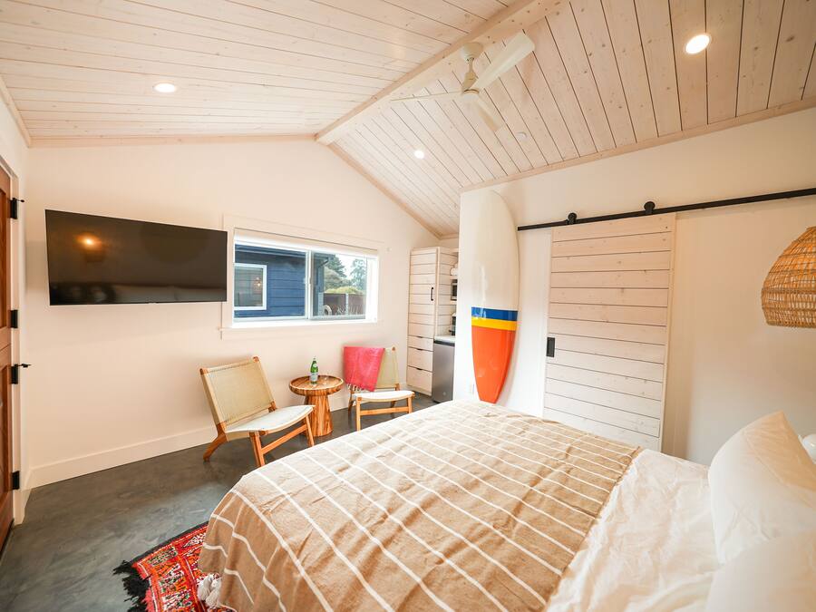 A bedroom with a bed, a TV, a window, a chair, a small table, and a wardrobe.