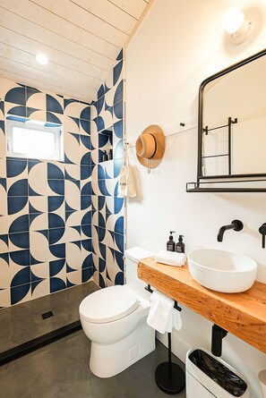 Une salle de bain moderne avec un carrelage aux motifs géométriques, un meuble-lavabo en bois, un grand miroir et des toilettes blanches.