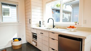 A modern kitchen with wooden cabinets, a stainless steel dishwasher, and a window with a view of the backyard. - Surf Lodge (Stinson Beach)