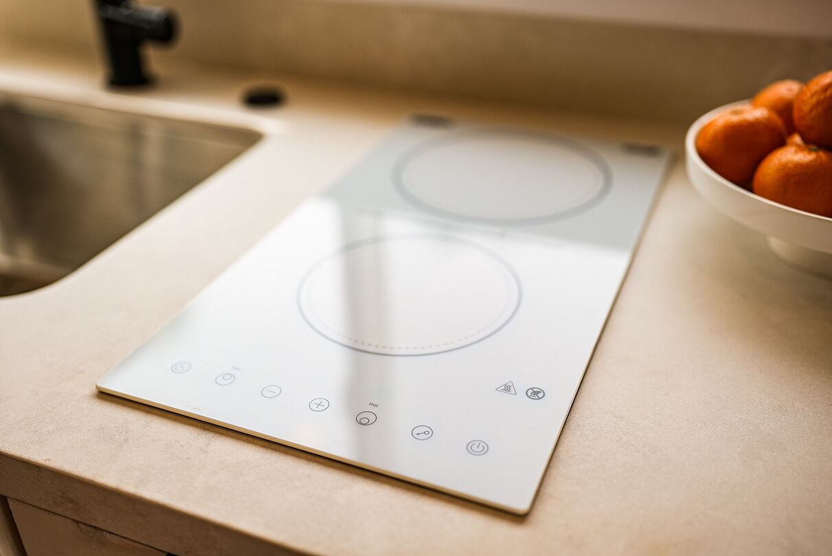 Une cuisine équipée d’une plaque de cuisson à induction, d’un évier et d’un saladier rempli d’oranges posé sur le plan de travail.
