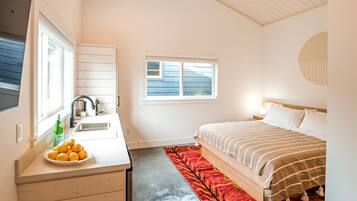 A compact bedroom with a bed, a small desk with a sink, a window, and a red rug.