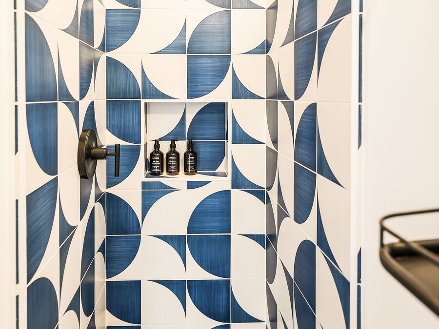 A bathroom with a geometric tile pattern, a shower, and a sink with toiletries.