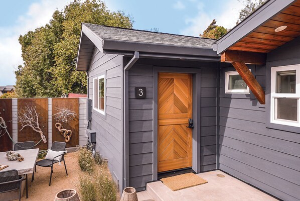 Une maison avec une porte en bois, un petit porche doté d’un banc et une cour arrière clôturée.