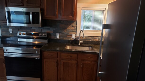 A kitchen with wooden cabinets, a stainless steel microwave, oven, and refrigerator. - Camp Fishbone - Our place at the Lake (Freeport)