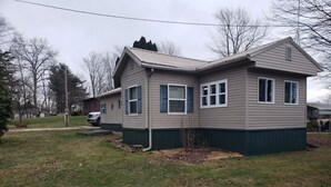 A two-story house with a sloped roof, a front porch, and a small front yard. - Camp Fishbone - Our place at the Lake (Freeport)