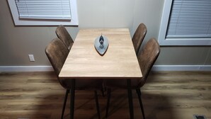 A dining table with four chairs, a decorative item on the table, and a window with blinds. - Camp Fishbone - Our place at the Lake (Freeport)