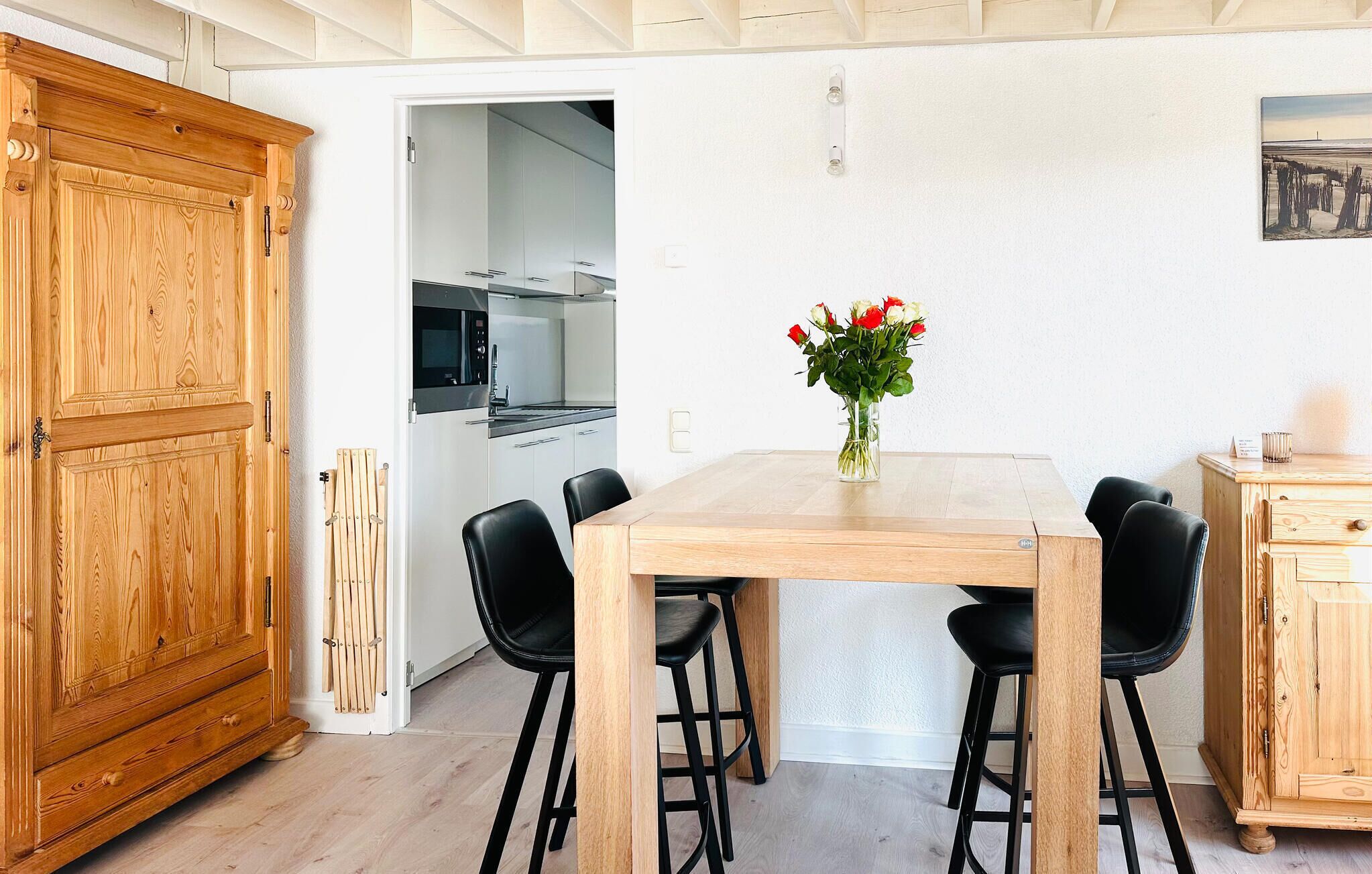 A dining area with a wooden table and four black chairs, a vase of flowers, and a wooden cabinet to the left.