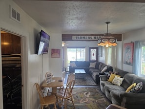 A living room with a sofa set, a coffee table, a TV mounted on the wall, and a 'Farmers Market' sign. - Campau Lake Sunnydays Retreat | 3BR | Spa (Alto)