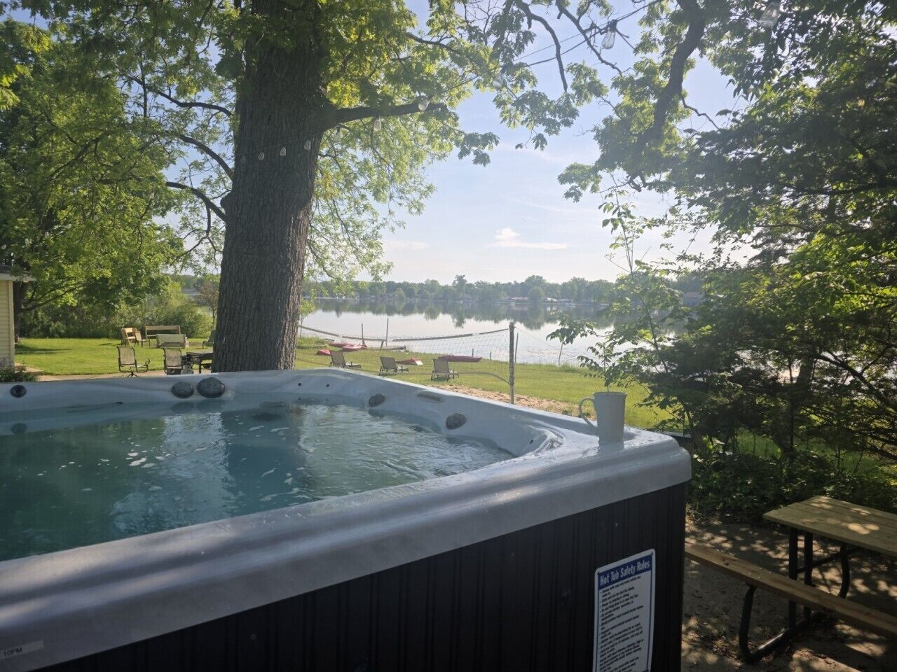 Een hottub met een veiligheidsteken, omringd door bomen en uitzicht op een meer.