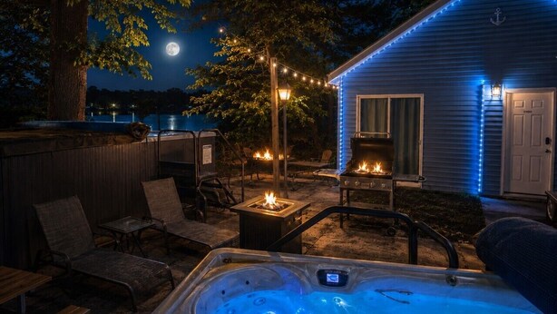 A backyard with a hot tub, outdoor seating, and a house with blue exterior lighting.