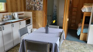A compact kitchen with wooden cabinetry, a dining table with chairs, and a small seating area with a bench. - Queenstown Copper Country Cabins (Queenstown)