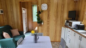 A compact living space with a dining table, chairs, a sofa, a kitchen area with a microwave, and a clock on the wall. - Queenstown Copper Country Cabins (Queenstown)