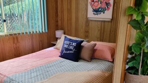 A wooden-paneled room with a bed, a window with blinds, a wall-mounted painting, and a potted plant. - Queenstown Copper Country Cabins (Queenstown)