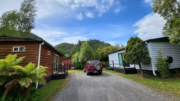 A gravel driveway leading to a row of cabins with a forested hillside in the background. - Queenstown Copper Country Cabins (Queenstown)
