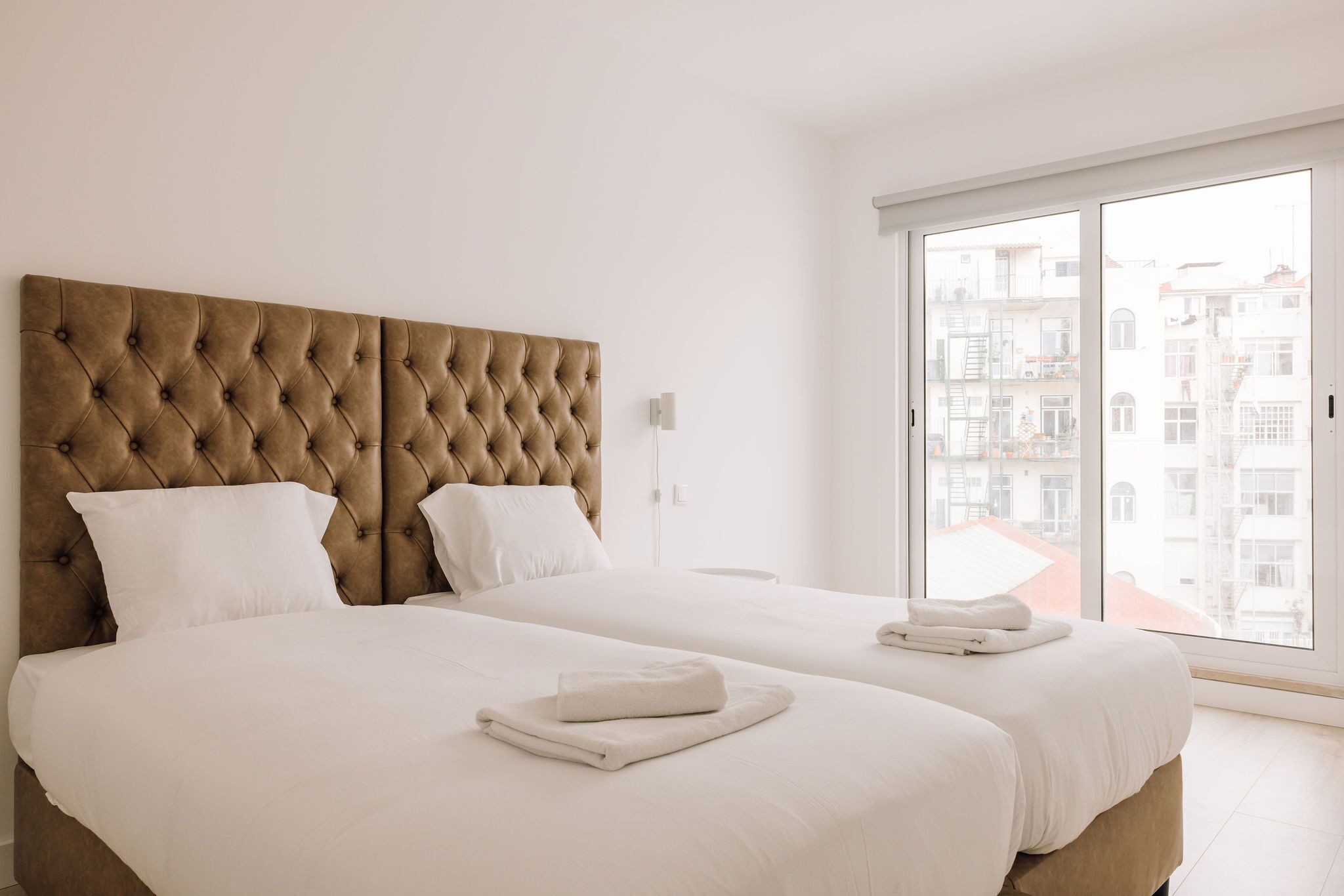 Ein Hotelzimmer mit zwei Betten, einem großen Fenster und Blick auf Gebäude.