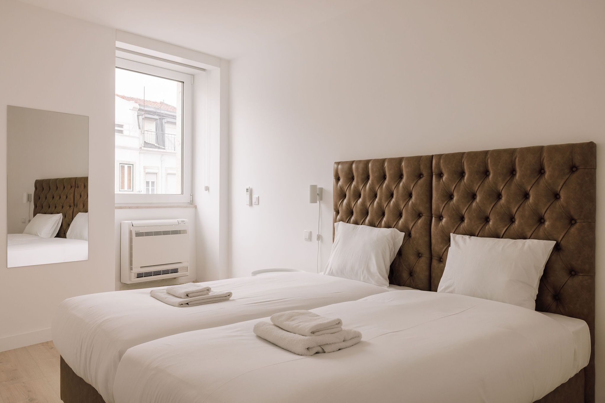 A hotel room with a large bed, a window, a wall-mounted air conditioner, and a mirror.