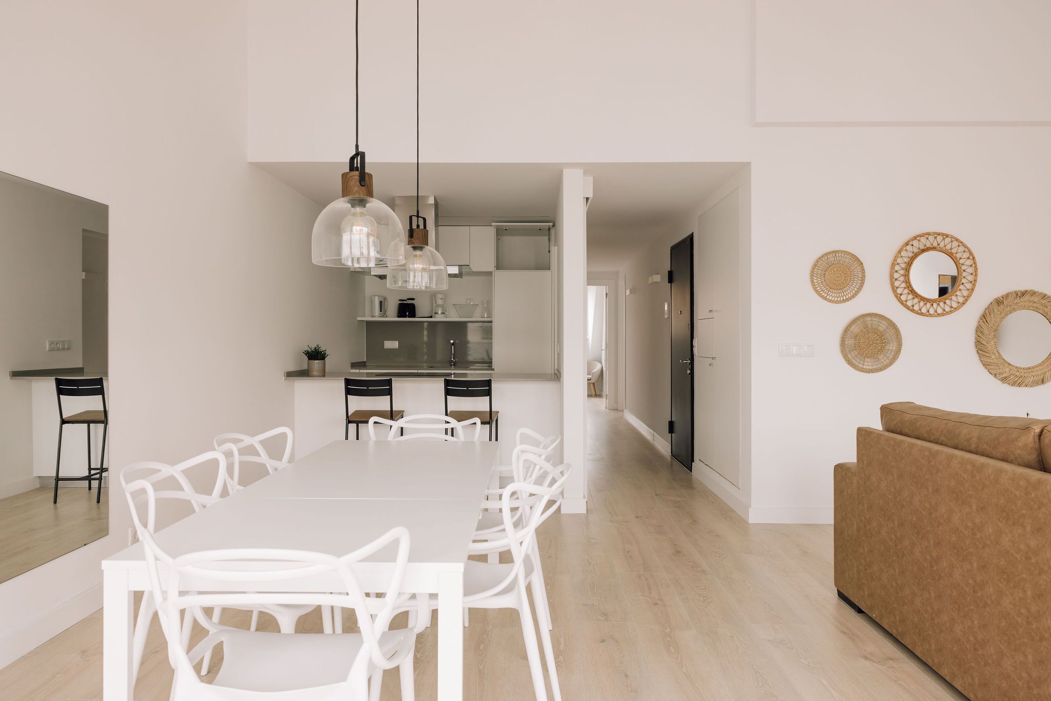 A modern kitchen with white cabinetry, a dining area with a white table and chairs, and a brown sofa in a living area.