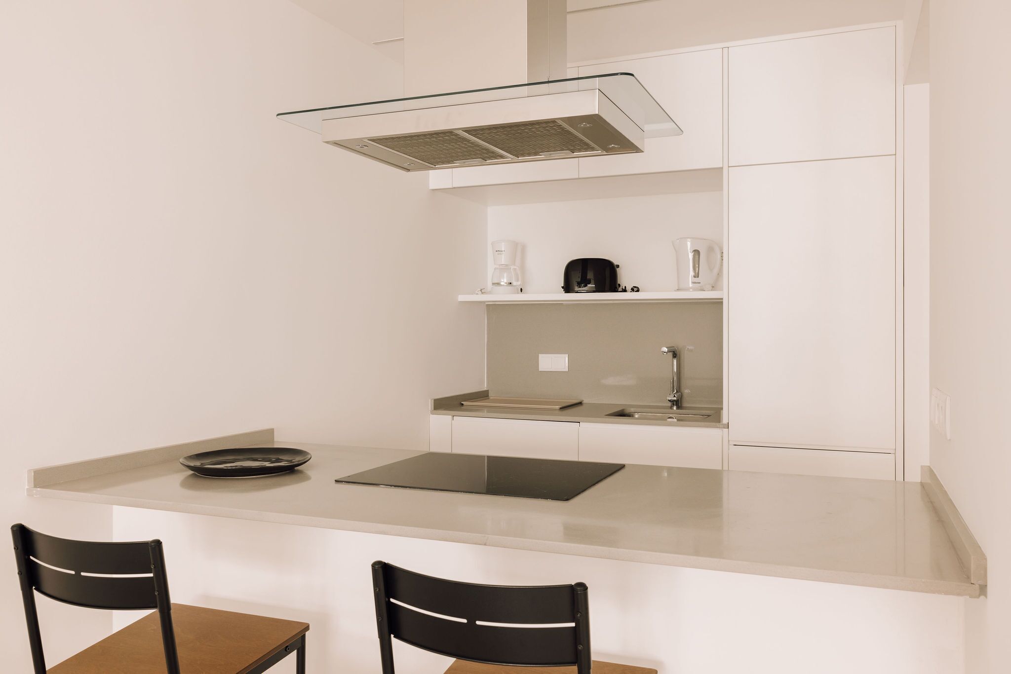 Una cocina compacta con una isla, dos sillas, una cafetera y un hervidor.