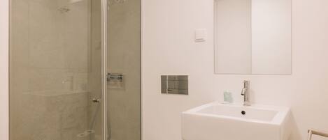 Un baño moderno con cabina de ducha de vidrio, un lavabo blanco y un espejo sobre el lavabo.