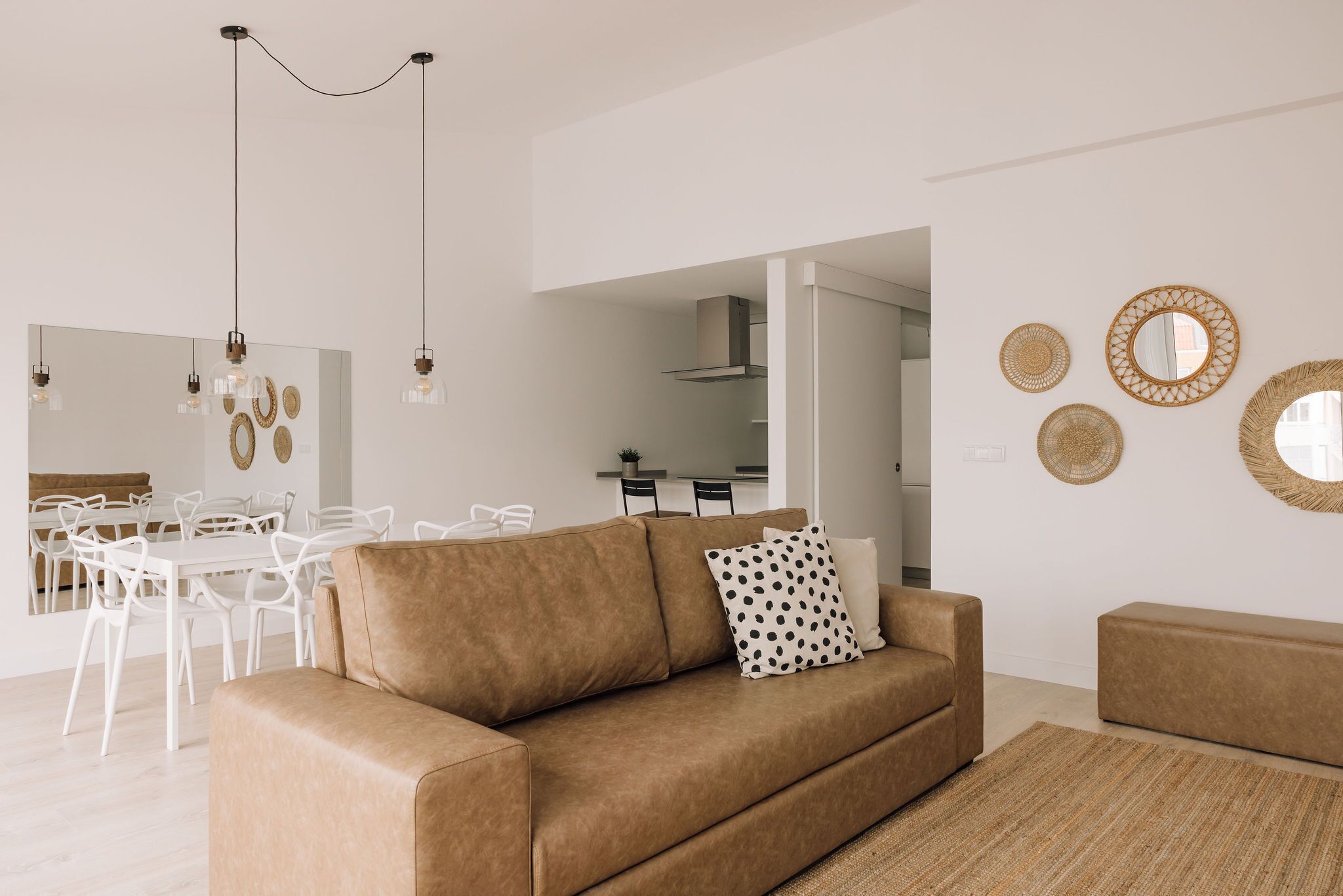 Una sala de estar moderna con un sofá marrón, sillas blancas, una mesa de comedor y una cocina al fondo.