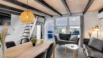 En moderne stue med et træspisebord, en sofa og et sofabord. Der er en trappe til et niveau ovenover, og store vinduer giver naturligt lys.