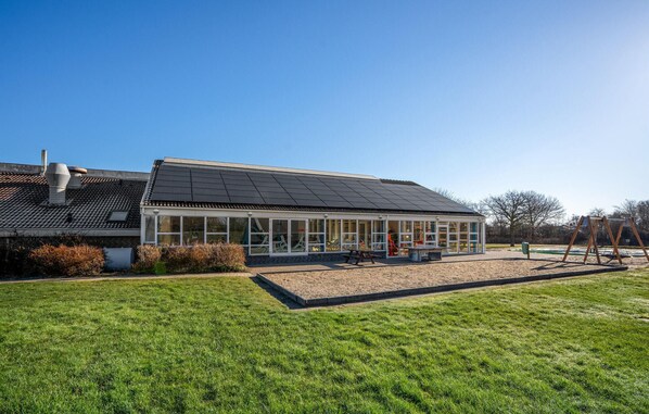 A modern building with a glass enclosure, a solar panel roof, and a playground area.