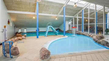 En indendørs swimmingpool med rutsjebane, klippeformationer og udsigt til det fri gennem store vinduer.