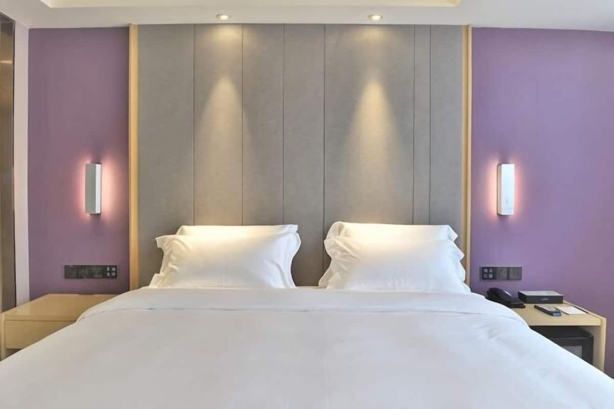 A hotel room with a large bed, two bedside tables, and wall-mounted lighting.