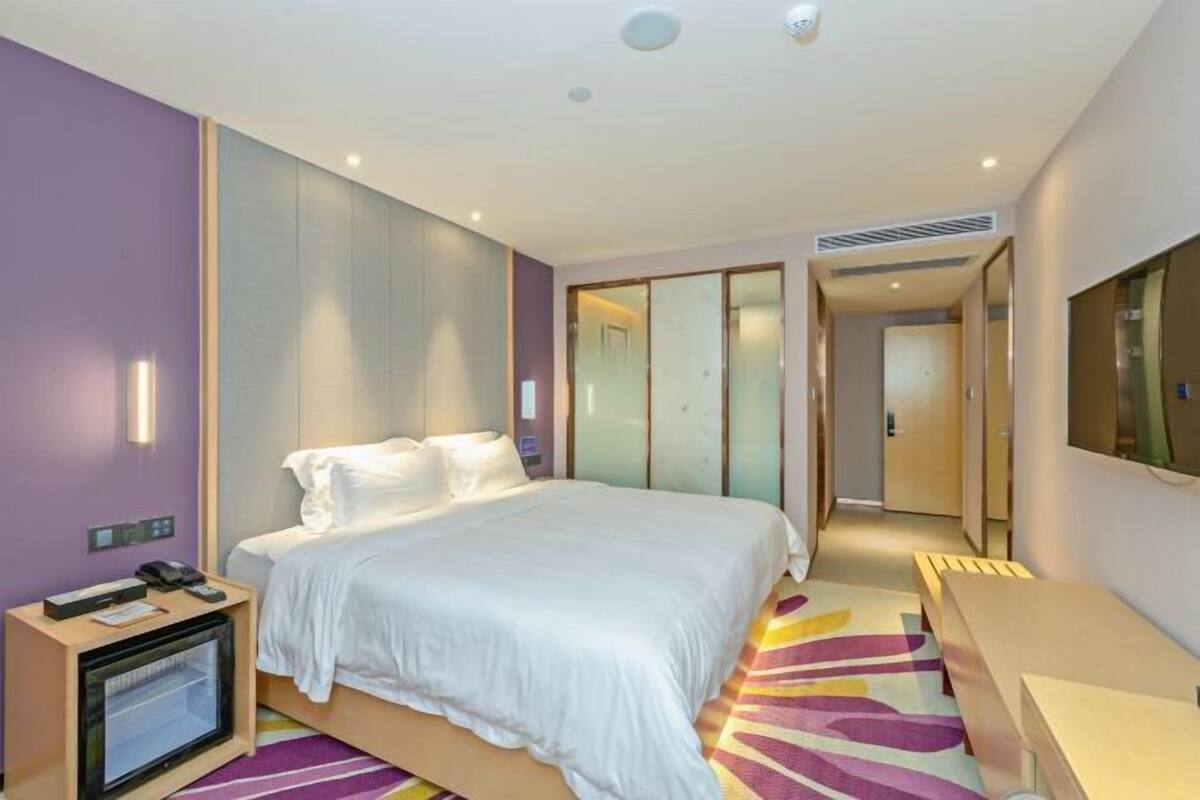 A modern hotel room with a large bed, bedside table, and a television.