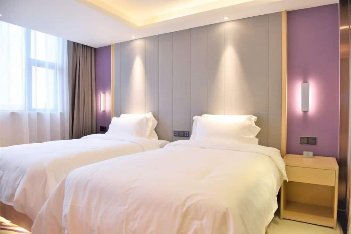 A hotel room with two beds, a bedside table, a nightstand, and a wall-mounted light fixture.