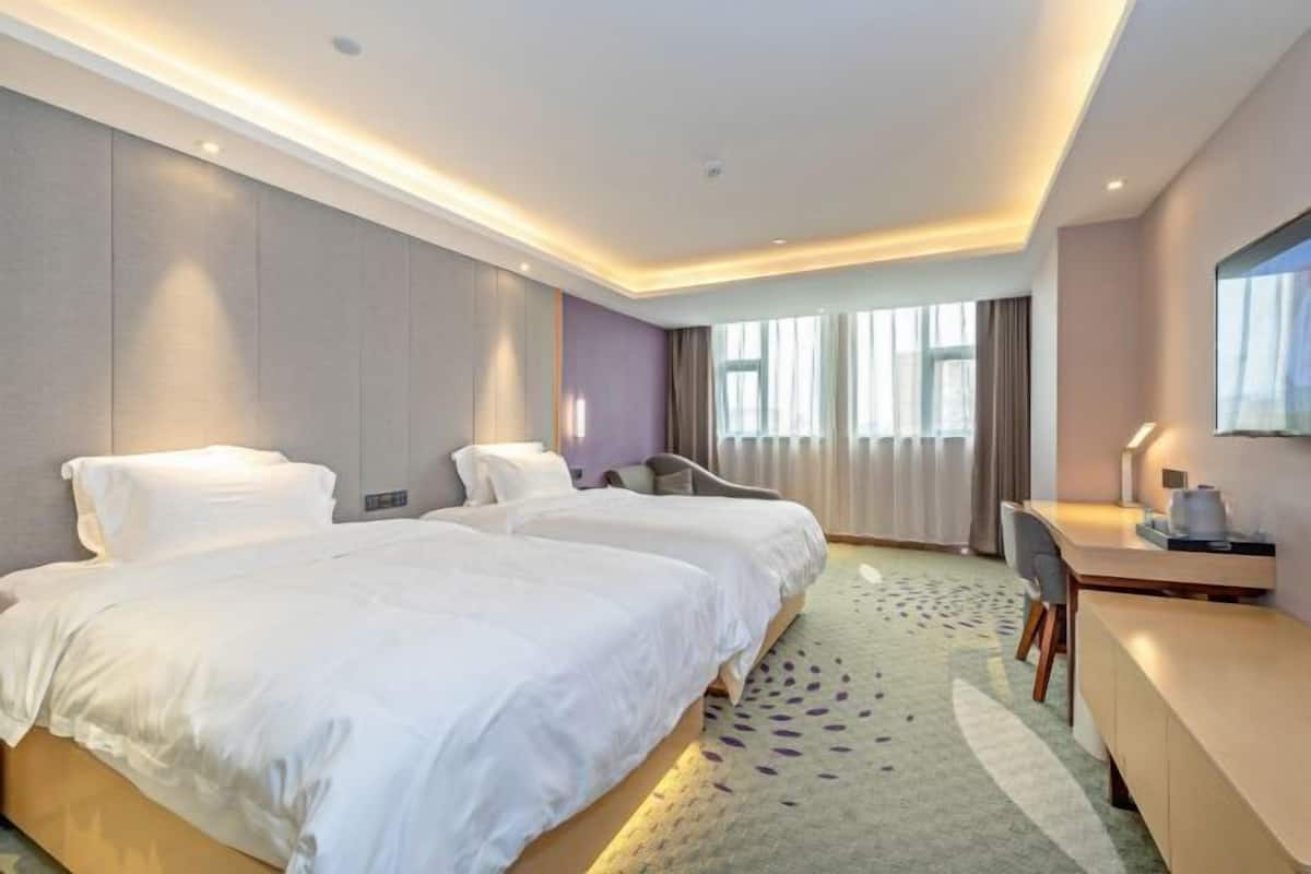 A hotel room with two beds, a desk, a chair, and a large window with curtains.