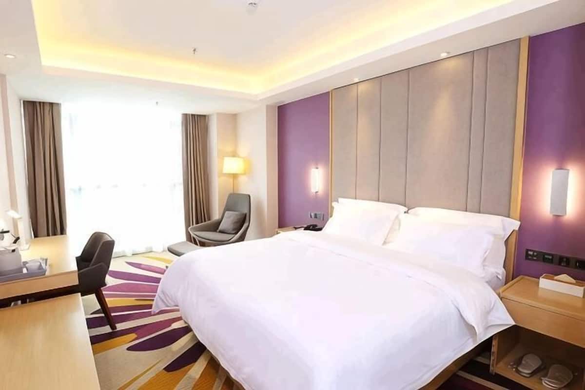 A hotel room with a large bed, a desk, a chair, and a view of the outdoors.