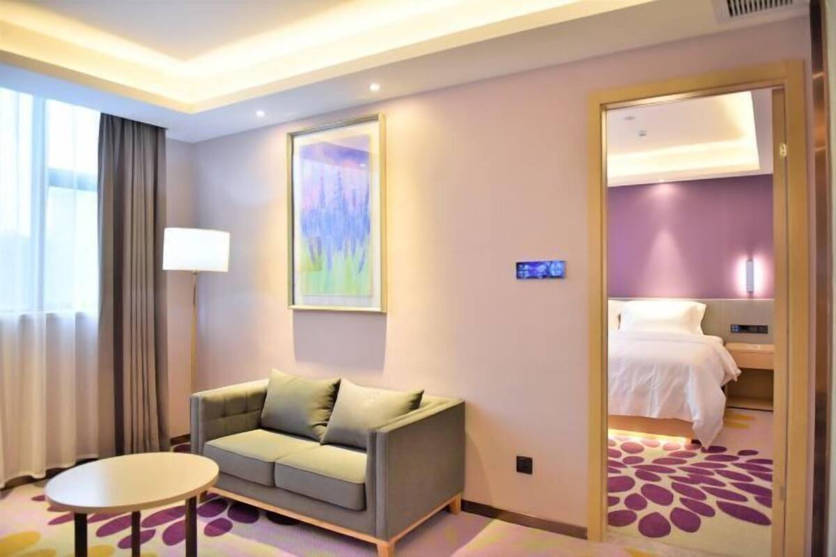 A hotel room with a sofa, a small table, a bed, and a painting on the wall.
